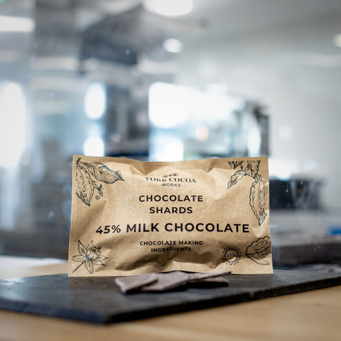 Bag of 45% milk chocolate shards on a slate counter with blurred factory background