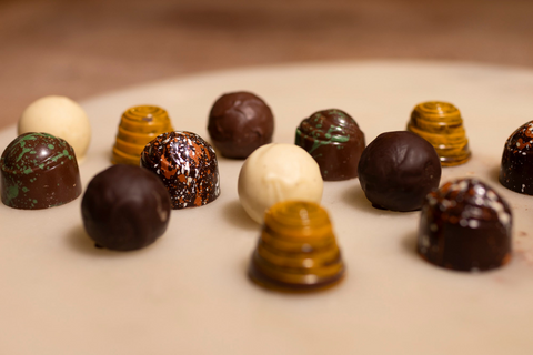 A collection of chocolate truffles on a white marble background with milk, white, dark, honeycomb, lemon verbena and orange blossom truffles.