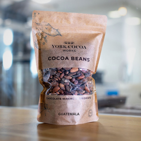 Bag of York Cocoa Works cocoa beans on a wooden surface with a blurred factory background