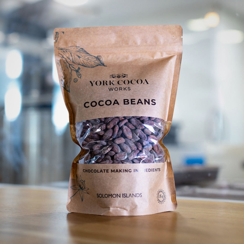 Bag of York Cocoa Works cocoa beans on a wooden surface with a blurred factory background