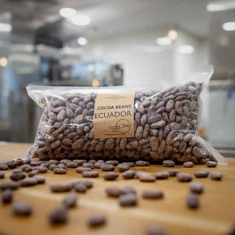 Packaged cocoa beans from Ecuador on a wooden surface with a blurred factory background