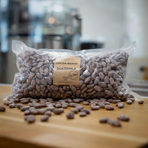 Bag of York Cocoa Works cocoa beans with a Guatemala label on a wooden surface with a blurred factory background