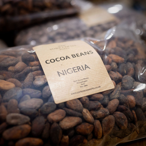 Bag of cocoa beans with a label indicating 'Cocoa Beans Nigeria' on a blurred background.