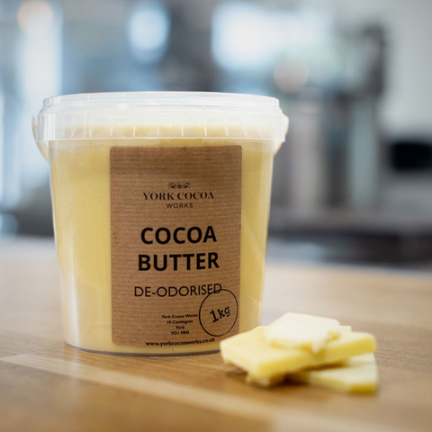 Container of deodorized cocoa butter on a wooden surface with a blurred factory background