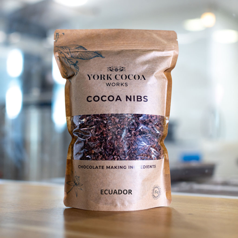 Bag of York Cocoa Works cocoa nibs on a wooden surface with a blurred factory background