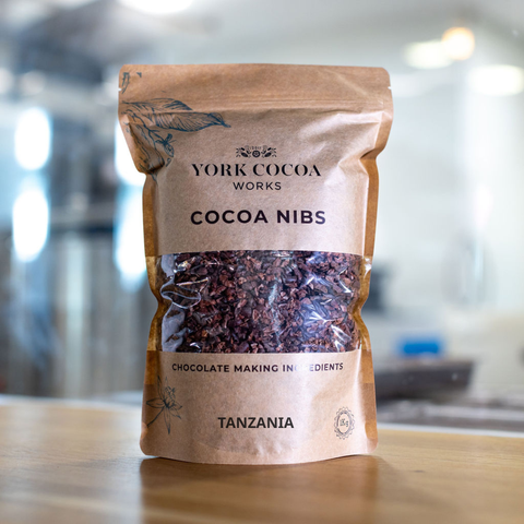 Bag of York Cocoa Works cocoa nibs on a wooden surface with a blurred factory background