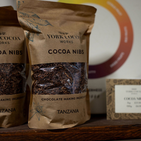 Packages of York Cocoa Works cocoa nibs on a wooden shelf with a blurred background.