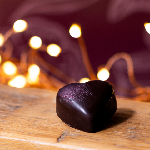 A salted caramel truffle heart resting on a wooden surface, with warm fairy lights blurred in the background.