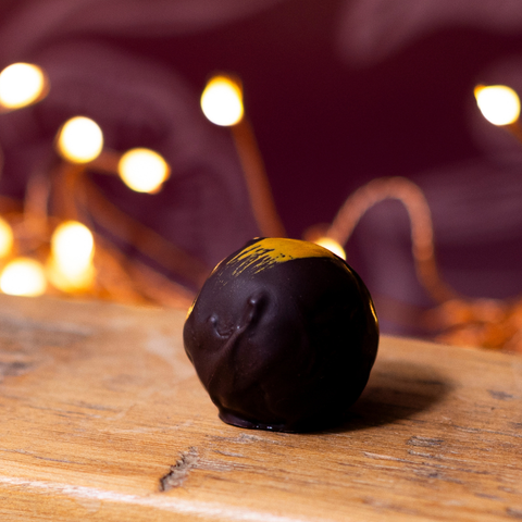 A single cocoa fruit caramel chocolate sphere, resting on a wooden surface with warm blurred fairy lights in the background.