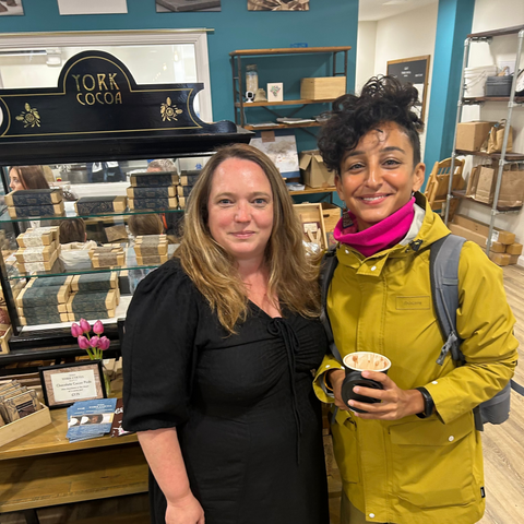 Two women standing together in a store with shelves and products in the background.