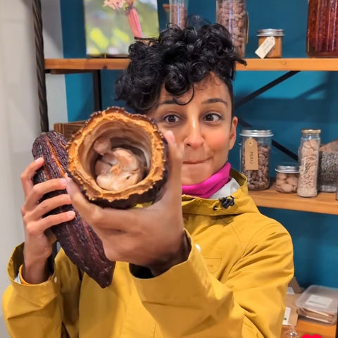Person in a yellow jacket holding an open Cocoa Pod with a shelf of jars in the background