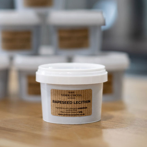 Container of rapeseed lecithin with a York Cocoa Works label on a wooden surface and a blurred background