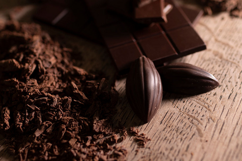 Hot Chocolate flakes, two chocolate cocoa pod pieces and dark chocolate bars on a wooden surface.